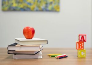 Stacked books with apple on top. Some colour pencils and stacked blocks on the table.