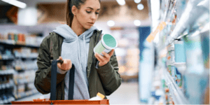 Focused woman in grocery store aisle attentively reading the nutrition facts label on a food package to make informed dietary choices