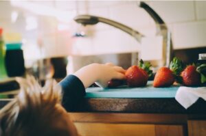 Close-up of a child's hand reaching for fresh strawberries on a kitchen countertop