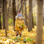 A young child joyfully playing in a park, tossing up a pile of crisp autumn leaves.