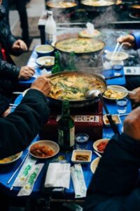 atrons enjoying a communal Korean street food experience with a bubbling hot pot and side dishes, reflecting the social and cultural essence of dining in Korea.