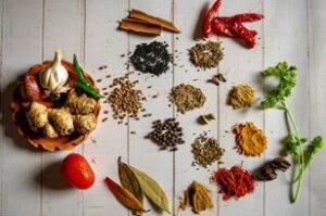  An assortment of vibrant spices and herbs laid out on a wooden table, ingredients that form the foundation of many culturally rich and flavorful cuisines.