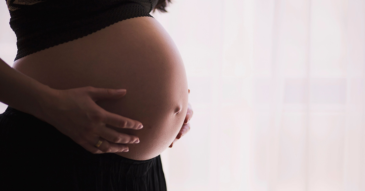 A pregnant person with their hands on their belly.