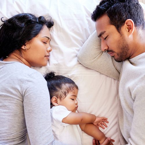 Young family sleeping together from above. Two parents sleeping with their baby girl. Little baby sleeping with her parents. Mother and father sleeping with a newborn baby. Multiracial family at home